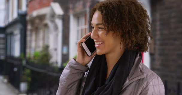 在伦敦公寓外的移动设备上 吸引人的千年聊天快乐地成为朋友 漂亮的黑人女性在手机上聊天 在住宅区街上笑着 — 图库视频影像