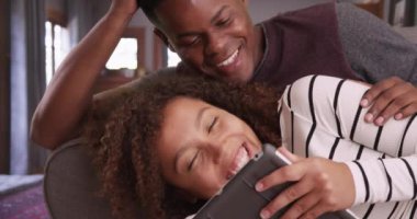 Siyah milenyum çifti tabletlerinde oyun oynarken yakın plan. Afrikalı erkek ve kadın kucaklaşıp kendi evlerinde film izliyorlar. 4k.