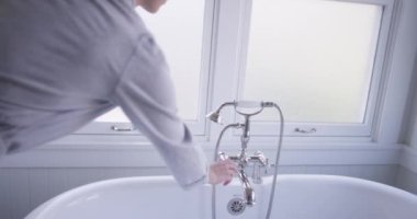 Çekici genç esmer kadın küvet musluğunu açıyor.