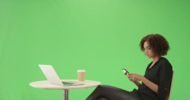 Genç siyahi bir kadın yeşil ekranda telefonuyla bir kafede oturuyor. Anahtar ya da birleşik olmak üzere yeşil ekranda.