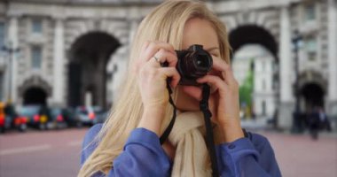 Londra 'daki St. James Park' ta tatil yapan mutlu sarışın beyaz kadın kamerasıyla fotoğraf çekiyor. Seyahat eden genç beyaz kadın İngiltere 'deki Deniz Kuvvetleri Kemeri yakınlarında fotoğraf çekiyor. 4k