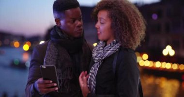 Yakışıklı siyahi adam Grand Canal 'ın yanında duruyor ve kız arkadaşı akıllı telefondan mesaj atıyor. Afro-Amerikan erkek Venedik 'te geceleri deniz kenarında 4G cep telefonu kullanıyor. 4k