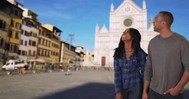 アフリカ系アメリカ人の男性と女性は イタリアのフィレンツェで休暇中に探索するのが大好きです フィレンツェを旅する若い黒人カップルは サンタ クローチェ大聖堂近くの観光スポットを楽しんでいます — ストック動画