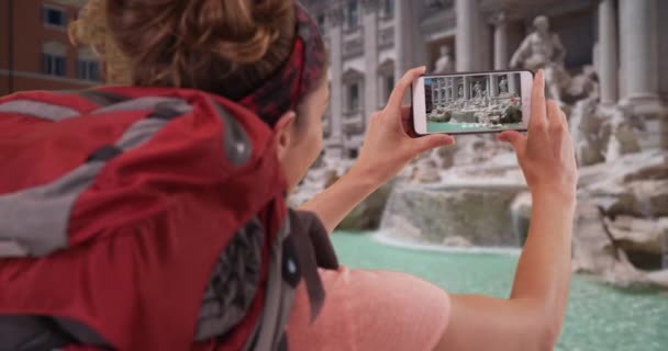 若いブルネットは彼女の電話でトレビの泉のビデオを撮るイタリアのローマを旅行しています 観光中にクリップを記録するローマの白い女性をバックパッキング — ストック動画