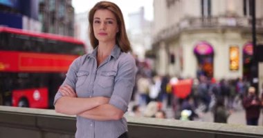 Ciddi bir beyaz kadın Londra, İngiltere 'de poz veriyor. Londra 'da kollarını kavuşturmuş genç beyaz bir bayan kameraya ciddi ciddi bakıyor. 4k