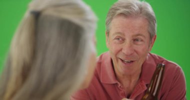 Yaşlı beyaz adam bir arkadaşıyla bira içiyor.