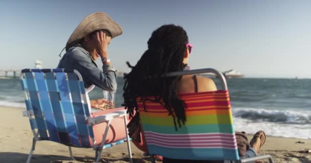 Μαύρες Γυναίκες Καλύτερες Φίλες Κάθονται Καρέκλες Στην Παραλία Πίνοντας Παγωμένο — Αρχείο Βίντεο