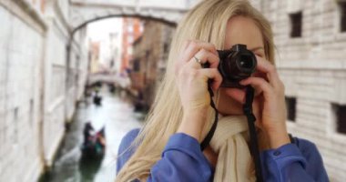 Venedik 'te dijital kamerasıyla gülümseyen beyaz kadın şehirde fotoğraf çekiyor. Güzel genç bayan turist Venedik, İtalya 'nın fotoğraflarını çekiyor. 4k