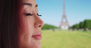 Eyfel Kulesi 'nin yanında dalgın Japon bir kadının yakın çekimi. Neşeli gülümseyen turist Paris 'teki hayatı düşünüyor. 4k