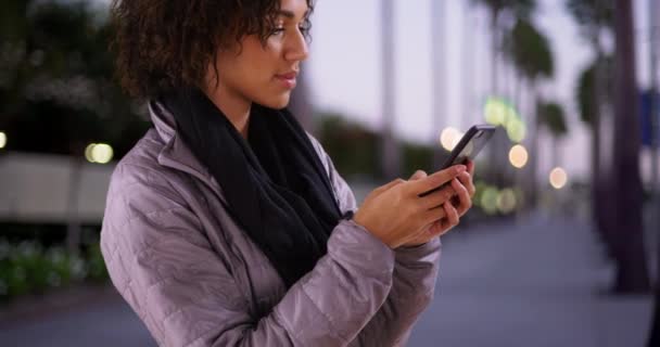 黑人女人在户外用智能手机发短信 单身黑人妇女站在人行道上使用智能手机 手机装置 — 图库视频影像