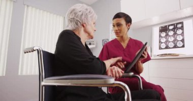 Genç hemşire tekerlekli sandalyedeki özürlü hastayla konuşuyor.