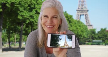 Mutlu olgun kadın geçenlerde çektiği Eyfel Kulesi 'nin fotoğrafını gösteriyor. Eyfel Kulesi 'nin yanında oturan neşeli beyaz kadın yakın zamanda çektiği bir fotoğrafı güvenle sergiliyor. 4k