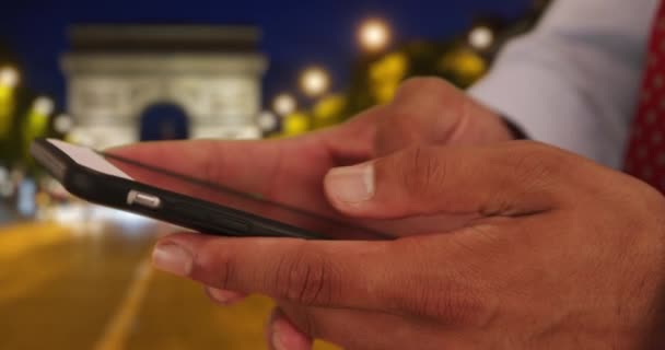 パリのスマートフォンでラテン語のビジネスマンのテキストを閉じます 夜には凱旋門近くの携帯電話で若い魅力的なプロの男性のメッセージングの閉鎖 — ストック動画