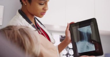 Afro-Amerikalı kadın doktor, yetişkin bir hastanın röntgenini inceliyor.