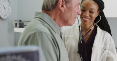 Dost canlısı kadın doktor, yaşlı hastanın nefes alışını dinliyor.