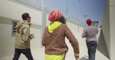 Aydınlık güneşli bir günde bir grup modern, çok ırklı arkadaş rıhtımda yürüyor.