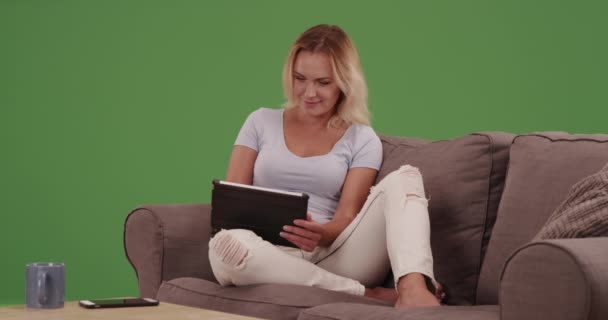 快乐的女人在沙发上的绿色屏幕上使用平板电脑 在绿色屏幕上键入或合成 — 图库视频影像