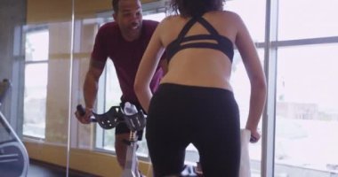 Sağlıklı uyumlu mutlu siyah ve İspanyol çift sabit bisiklet üzerinde pedal çevirirken ayağa kalkıyor.