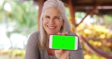 Elinde telefonla kameraya gülümseyen mutlu orta yaşlı kadın. Çekici orta yaşlı kadın yeşil ekranlı akıllı telefon gösteriyor..