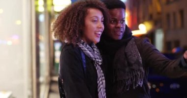 Paris 'te gece vakti vitrinlere bakan sevimli bir milenyum çifti. Mutlu çekici siyah çift şehirde eğleniyor. 4k