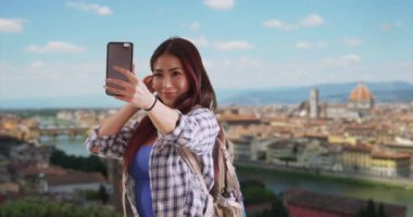 Arka planda Floransa manzarası olan selfie çeken mutlu Japon kadın. Gülümseyen turist yüzünü buruşturup kendi fotoğrafını çekiyor. 4k