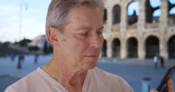 ローマでの休暇中の老人はコロッセオの前で電話をかける 電話で友人と成熟したカジュアルな男性のチャット — ストック動画