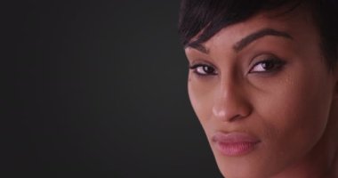 Gri arka planda güzel bir kadın kameraya bakıyor. 20 'li yaşlarda kısa saçlı Afro-Amerikan milenyumu..