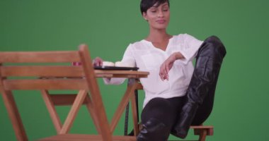 Çizmeli genç siyahi kadın yeşil ekrandaki kameraya bakan bir kafede ipad 'iyle şehvetli pozlar veriyor. Anahtar ya da birleşik olmak üzere yeşil ekranda.