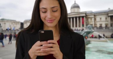 Trafalgar Meydanı 'nda gülümseyen Latin bir iş kadını cep telefonundan mesaj atıyor. Müze dışında gezici bir cep telefonuyla çekici İspanyol kadın mesajlarının sıradan portresi. 4k