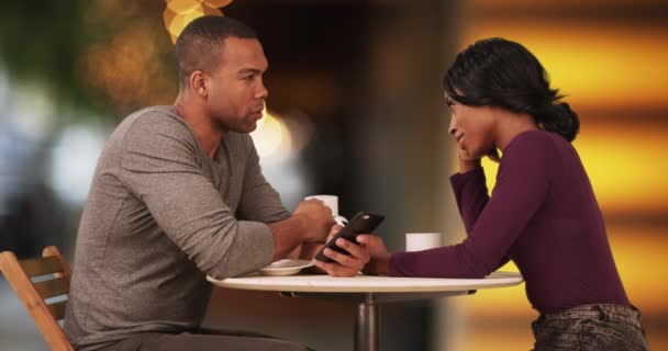 这对非洲裔美国夫妇约会时喝咖啡 在智能手机上浏览互联网 在咖啡馆里的黑人夫妇 发短信和聊天4K — 图库视频影像