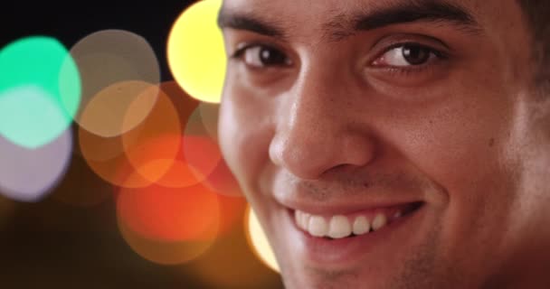 接近镜头的快乐拉丁男人看着相机在城市街道上的夜晚 西班牙千禧年的笑容和他身后的亮光 — 图库视频影像