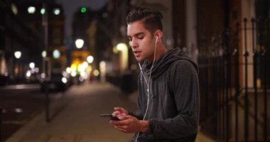 Milenyum kökenli İspanyol bir adam gece yarısı akıllı telefondan müzik dinliyor. Latin koşucu gece koşusuna ara veriyor ve şarkı dinliyor. 4k
