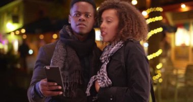 Genç Afrikalı Amerikalı çift akıllı telefonlarıyla bir taksi çağırıyorlar. Milenyum siyahi erkek ve kadın araba çağırır. 4k.