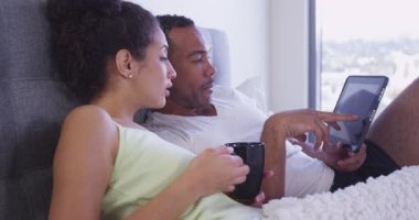 Latin ve Siyah çift yatakta tablet bilgisayara bakıyor. Yatakta oturuyor. Ağır çekim.