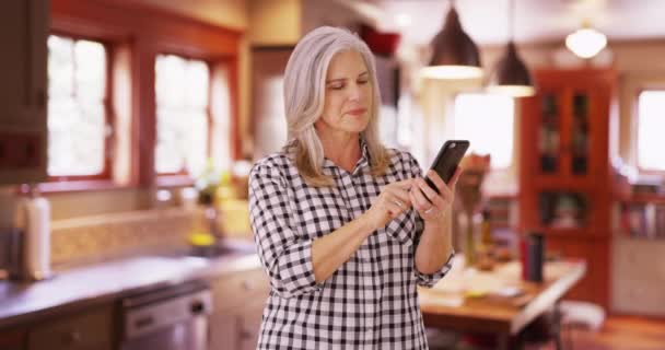 可爱的中年妇女用手机发短信 站在厨房里用智能手机的白人妇女 — 图库视频影像