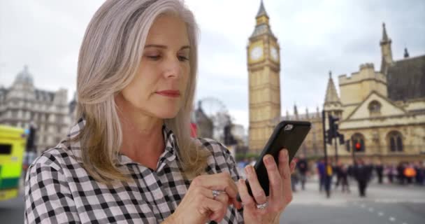 ロンドンの白人女性は市内観光中にテキストメッセージを送信します 熟女の休暇の女性は彼女のスマートフォンでウェブをサーフィンします 女性はロンドンのビッグ ベンの前で電話を使う — ストック動画
