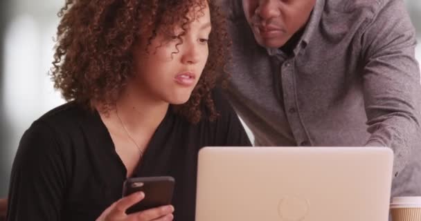 ラップトップのオフィスで働いている2人の黒人ビジネスの人々 アフリカ系アメリカ人男性は黒人女性に仕事を勧めます コンピュータと携帯電話を使った100万人の労働者 — ストック動画