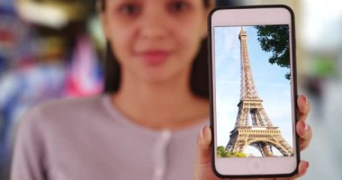 Genç İspanyol kadın akıllı telefondan Eyfel kulesinin görüntüsünü tutuyor. Çekici Latin milenyumu telefonunda Eyfel Kulesi 'nin resmini gösteriyor. 4k