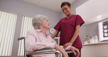 Genç çekici hemşire tekerlekli sandalyedeki yaşlı hastaya tablet gösteriyor.