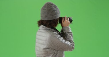 Siyah milenyum kızı, aynasız kamerasıyla yeşil ekranda kışlık giysileriyle fotoğraf çekiyor. Anahtar ya da birleşik olmak üzere yeşil ekranda.