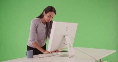 Millennial Latina 'nın profesyonel iş adamı masa başında duruyor ve masaüstü bilgisayarında çalışıyor. Şirket ofisindeki İspanyol iş kadını bilgisayara gülümsüyor. Birleşiklik veya anahtarlama için yeşil ekran. 4k