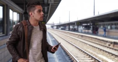 Bin yıllık yakışıklı Latin erkek tren istasyonunda bir araca selam veriyor. Elinde akıllı bir telefonla yola çıkmayı bekleyen İspanyol bir adam. 4k