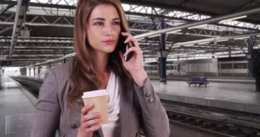 Genç, beyaz, profesyonel bir bayan kahve içerken bir meslektaşını arıyor. İyi giyimli beyaz kadın tren istasyonunda birini telefonla arıyor. 4k