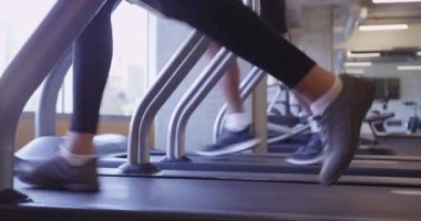 Spor salonunun düşük açılı manzarasında koşu bandında koşan iki kişiyi kapatın.