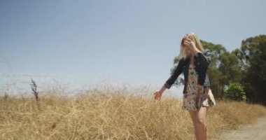 Genç hippi kadın toprak yolda yürüyor.