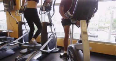 Sağlıklı siyah ve İspanyol erkekler ve kadınlar spor salonunda kardiyo makineleriyle çalışıyor.