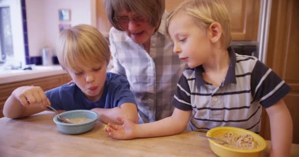 Ηλικιωμένοι Babysitter Βλέποντας Παιδιά Τρώνε Δημητριακά Πρωινό — Αρχείο Βίντεο