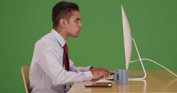 ヒスパニック系のビジネスマンは コンピュータ上で作業しながら 緑の画面上の携帯電話にテキストメッセージ 緑の画面でキーまたは構成されます — ストック動画