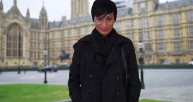Westminster, İngiltere 'de gezen genç, melez bir kadın. Kendine güveni tam. Westminster Sarayı 'nın önünde gururla duran çekici etnik turist. 4k