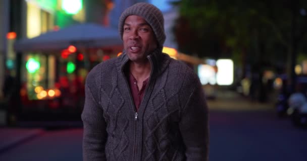 寒い夜に外に立つ冬服のアフリカ系アメリカ人の若者 寒い夜にセーターとビーニーを着た黒人男性の笑顔 — ストック動画